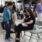 A lady wearing a blue shirt and fleece and a lady wearing a black shirt and pants interact at "A Pint For Kim" blood drive.