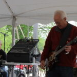 A man wearing a red sweater plays guitar.